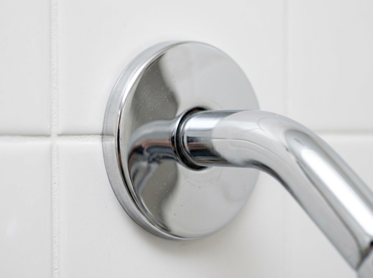 Close-up of a chrome shower arm escutcheon plate covering a wall pipe penetration
