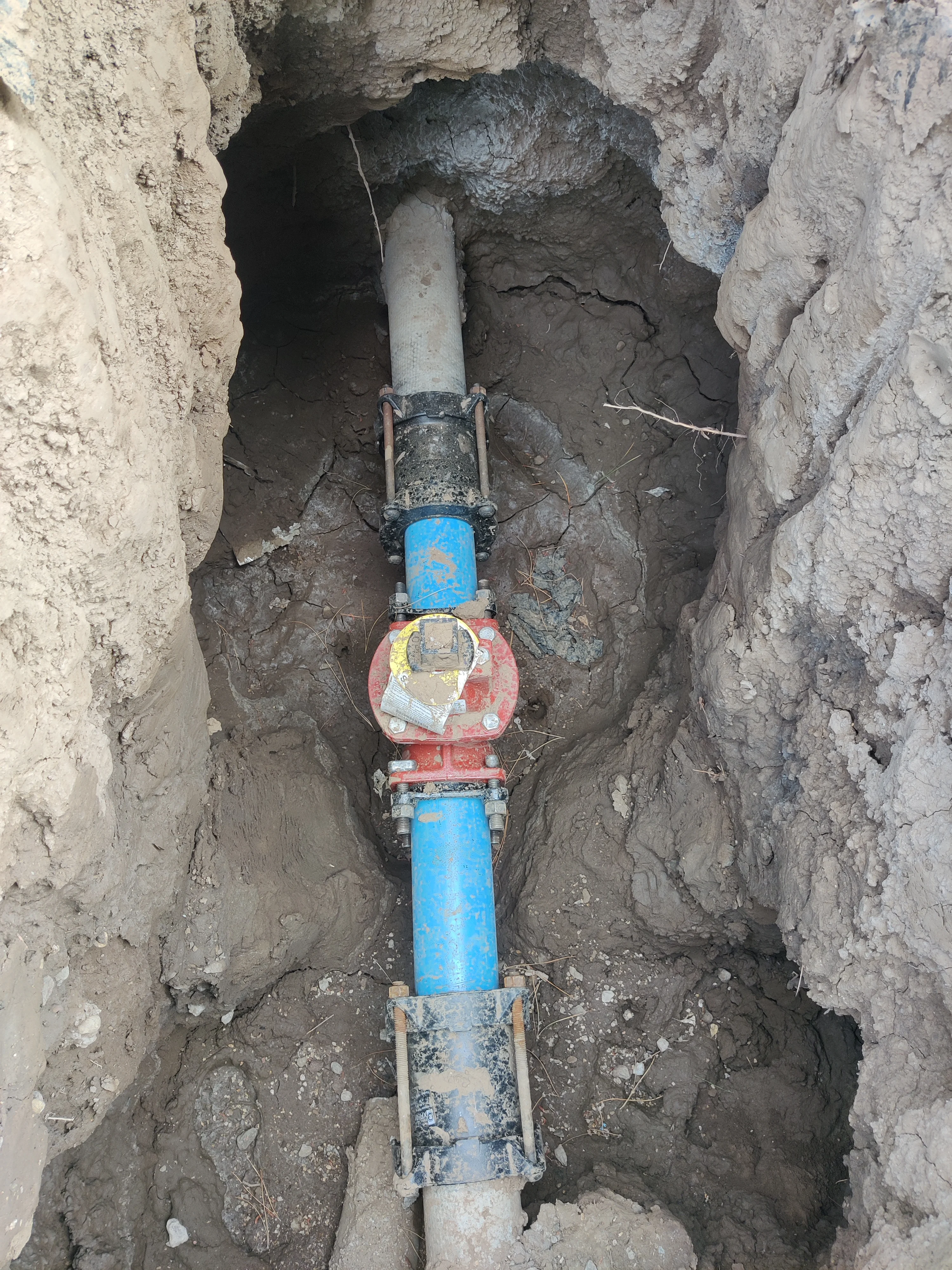 Blue PVC water main line with red ball valve and compression couplings installed in underground trench