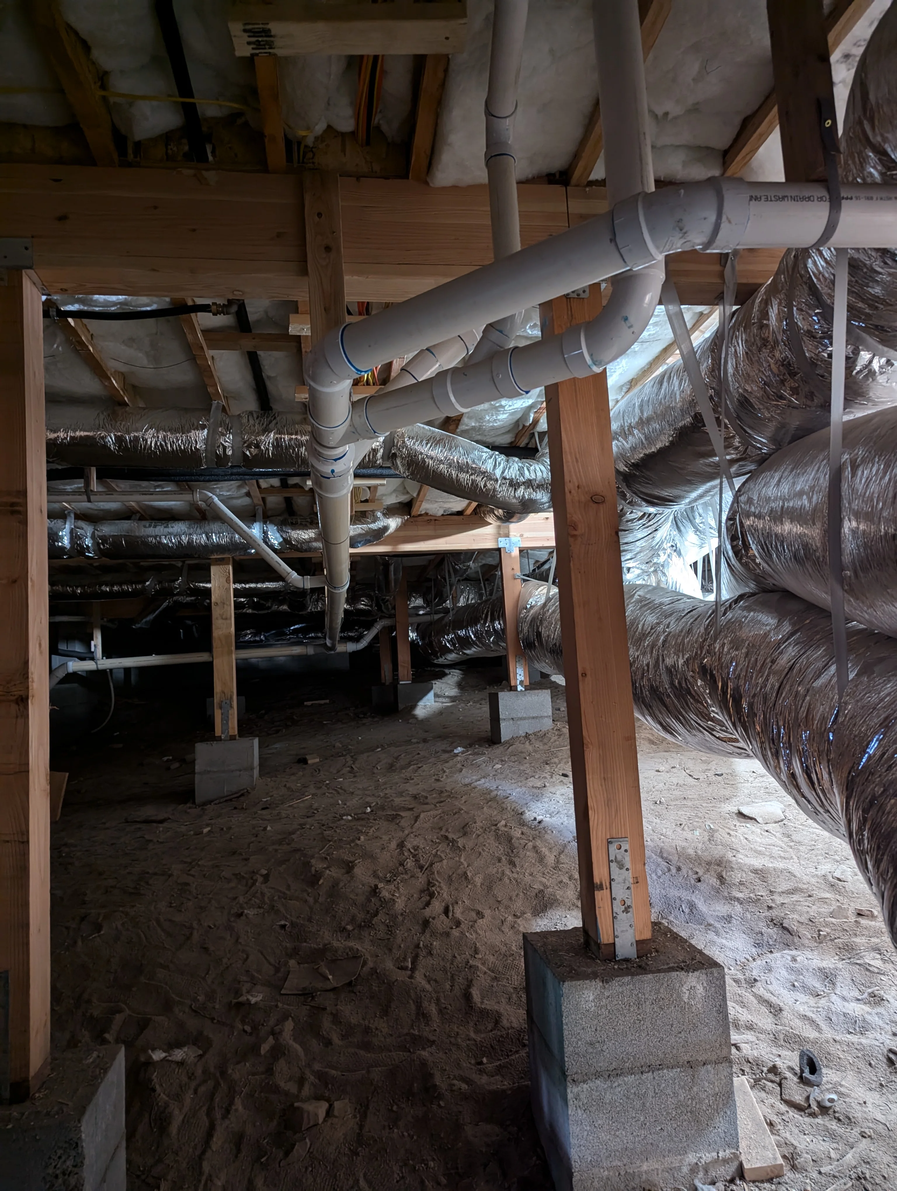 PVC plumbing lines and ductwork installed in crawlspace with wooden framing and concrete supports