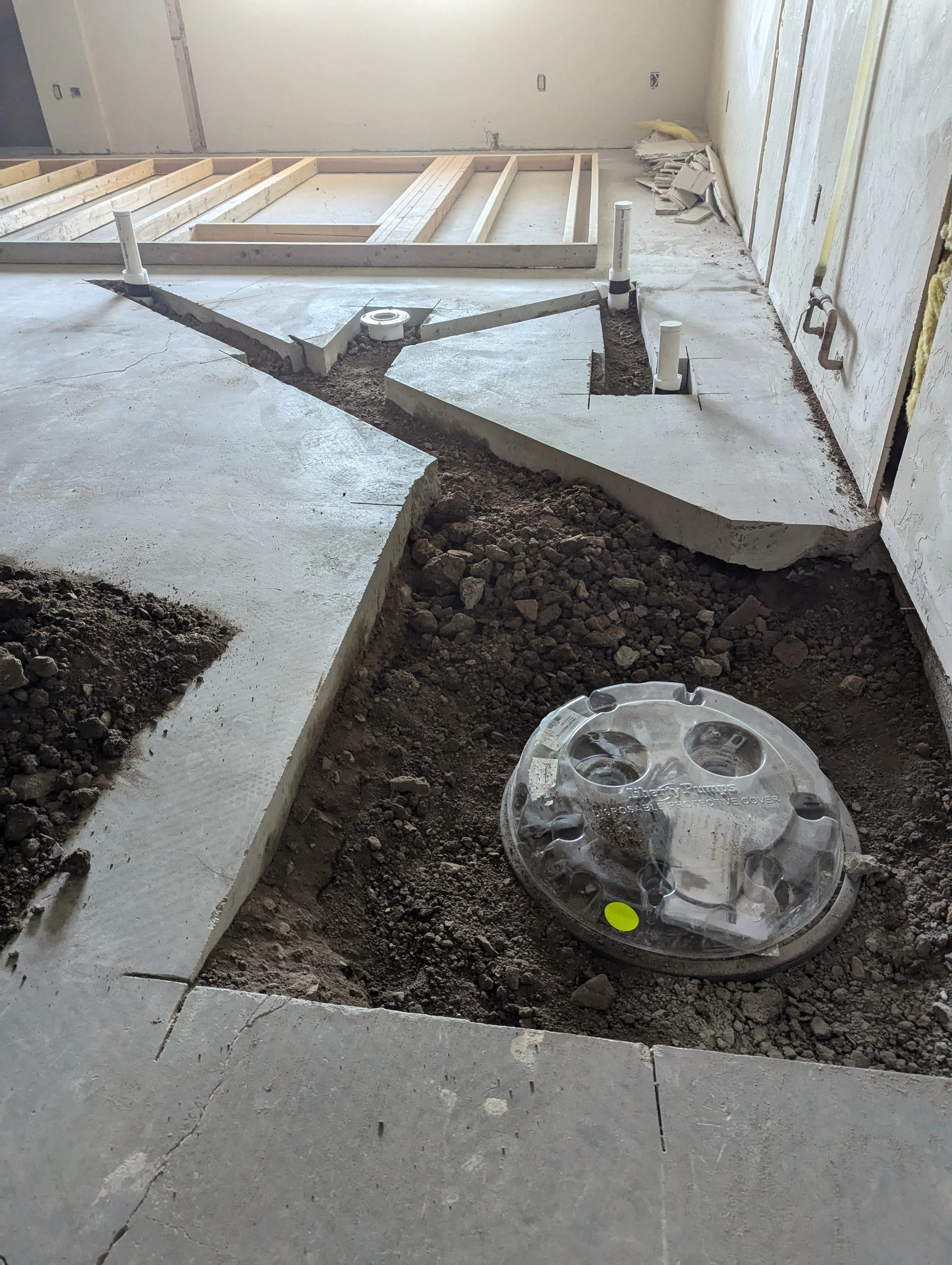 Concrete foundation with underground plumbing, septic access basin, and wooden floor framing