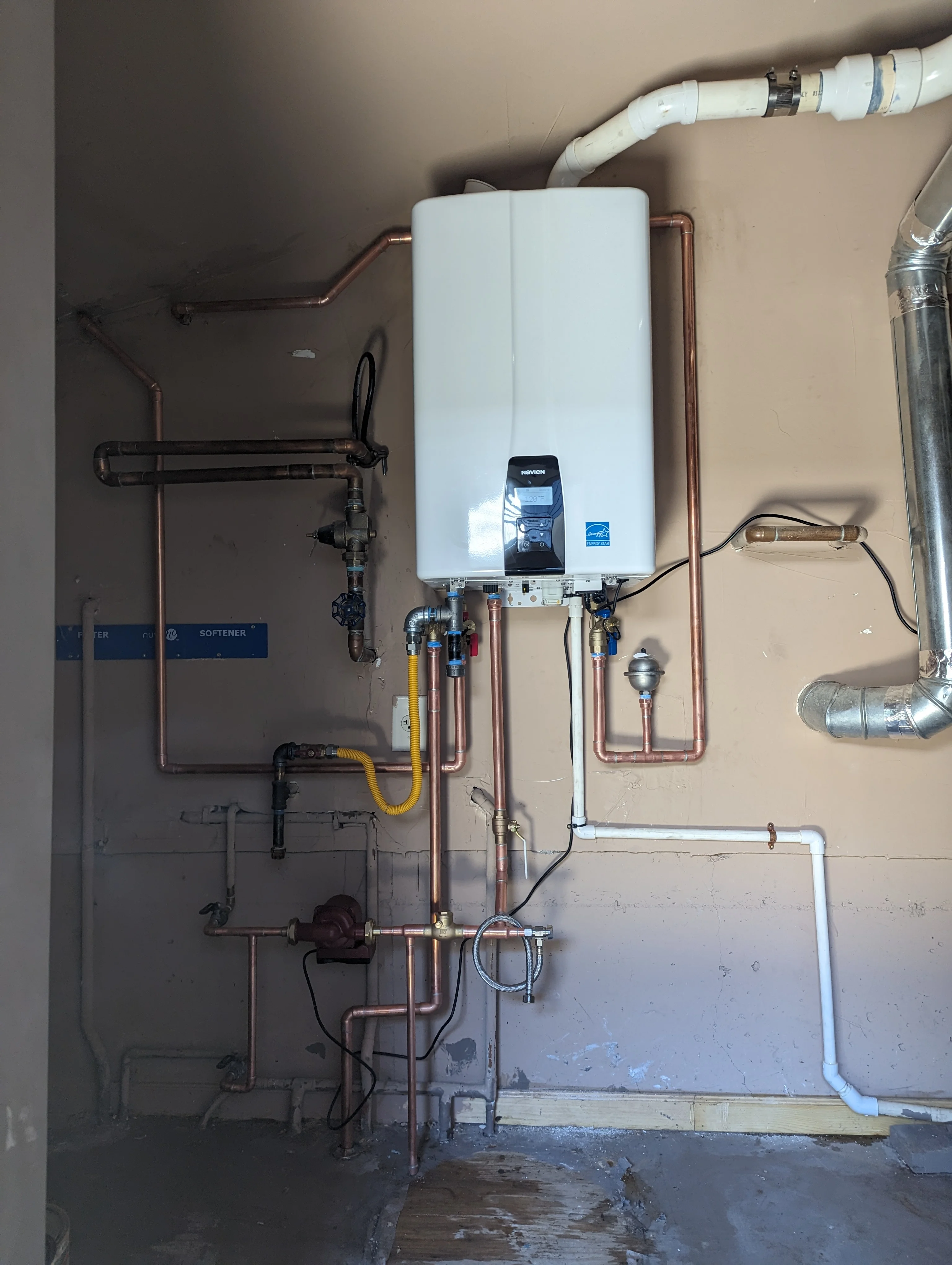 Tankless water heater with copper piping, valves, and PVC connections installed on wall
