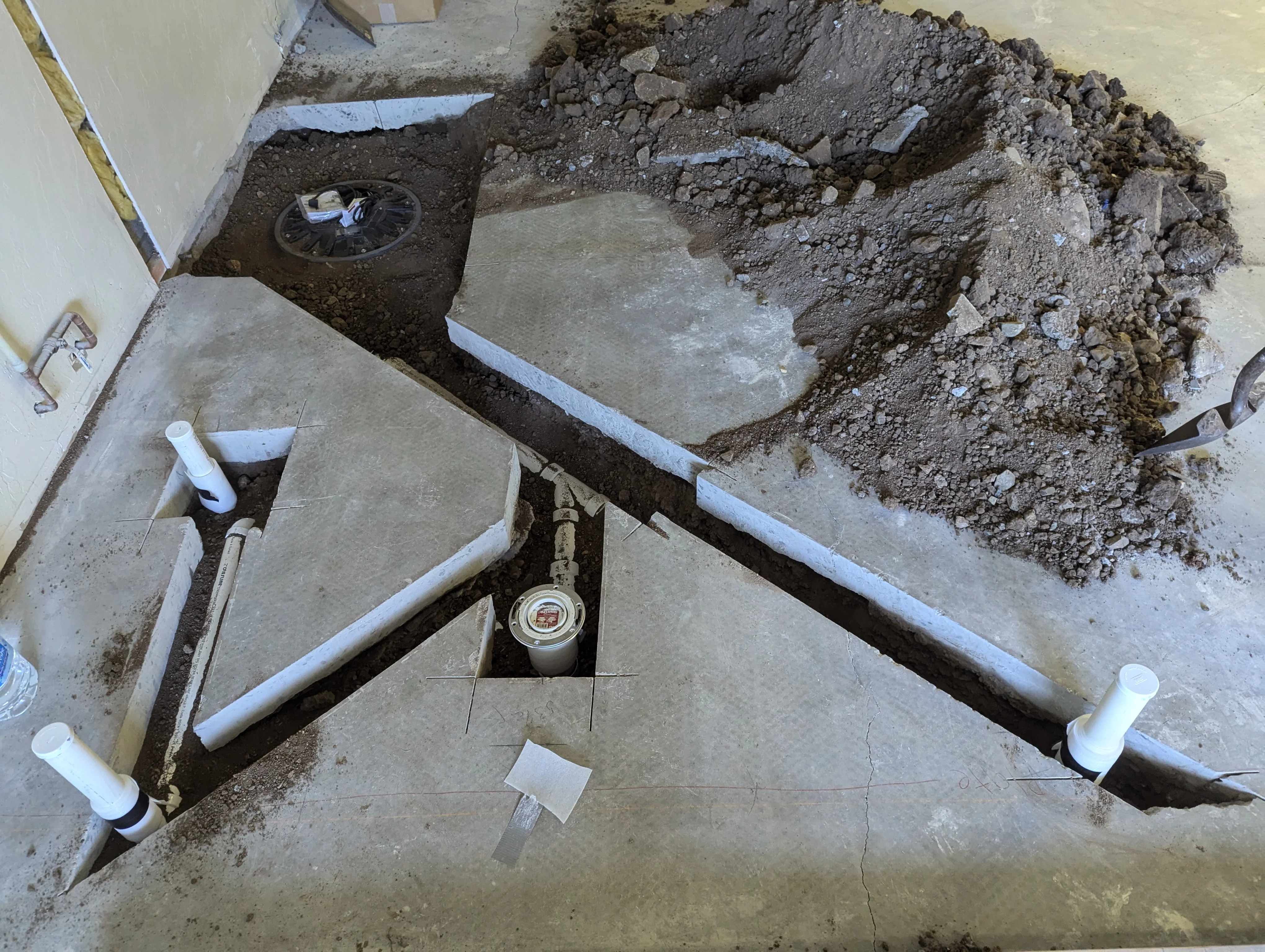 Underground PVC plumbing pipes and fittings installed in excavated trench with concrete foundation