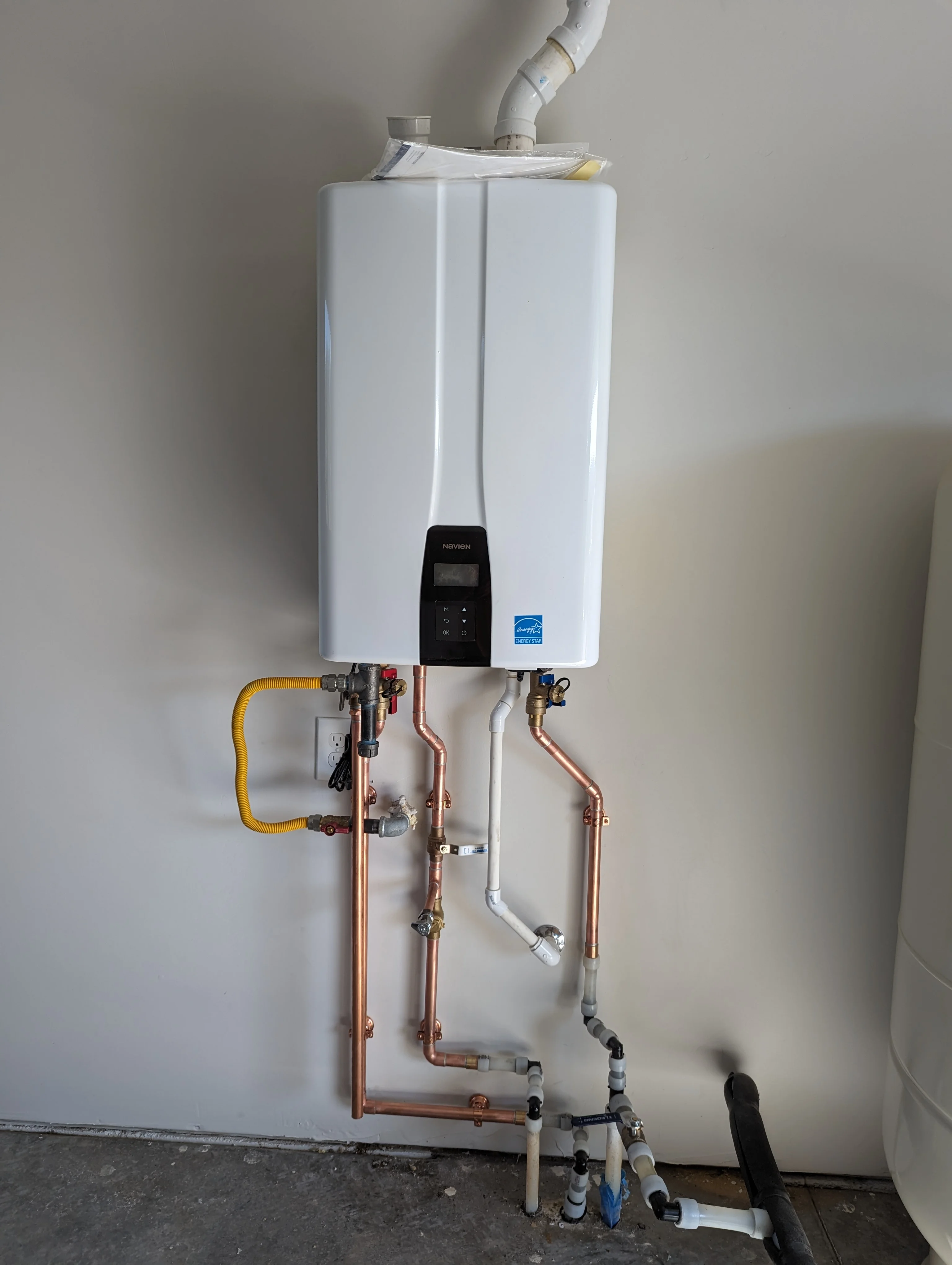 Tankless water heater with copper piping, PVC connections, and digital controls installed on wall