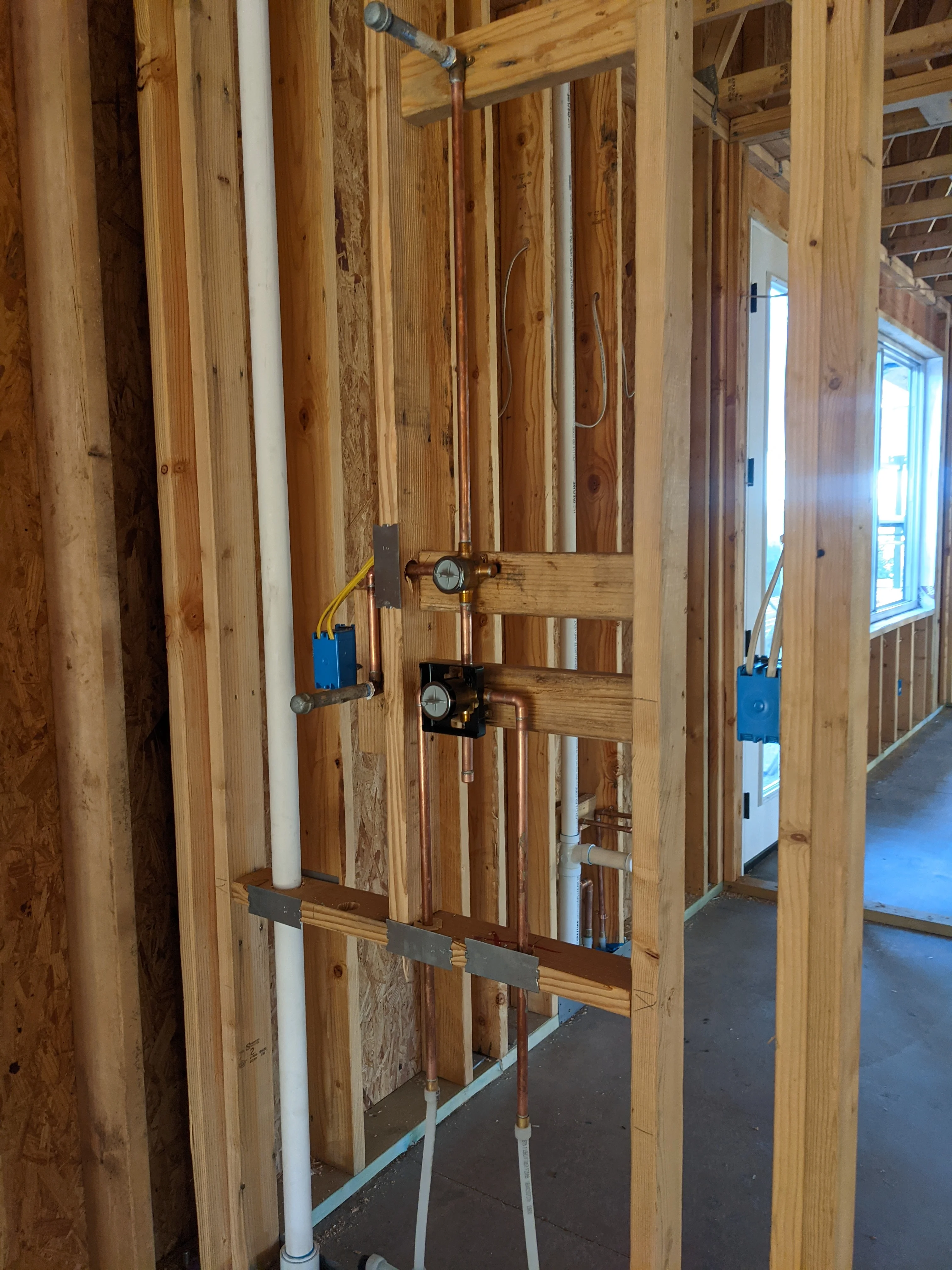 Rough-in plumbing with copper and PVC lines, shut-off valves, and pressure gauges in wood-framed wall
