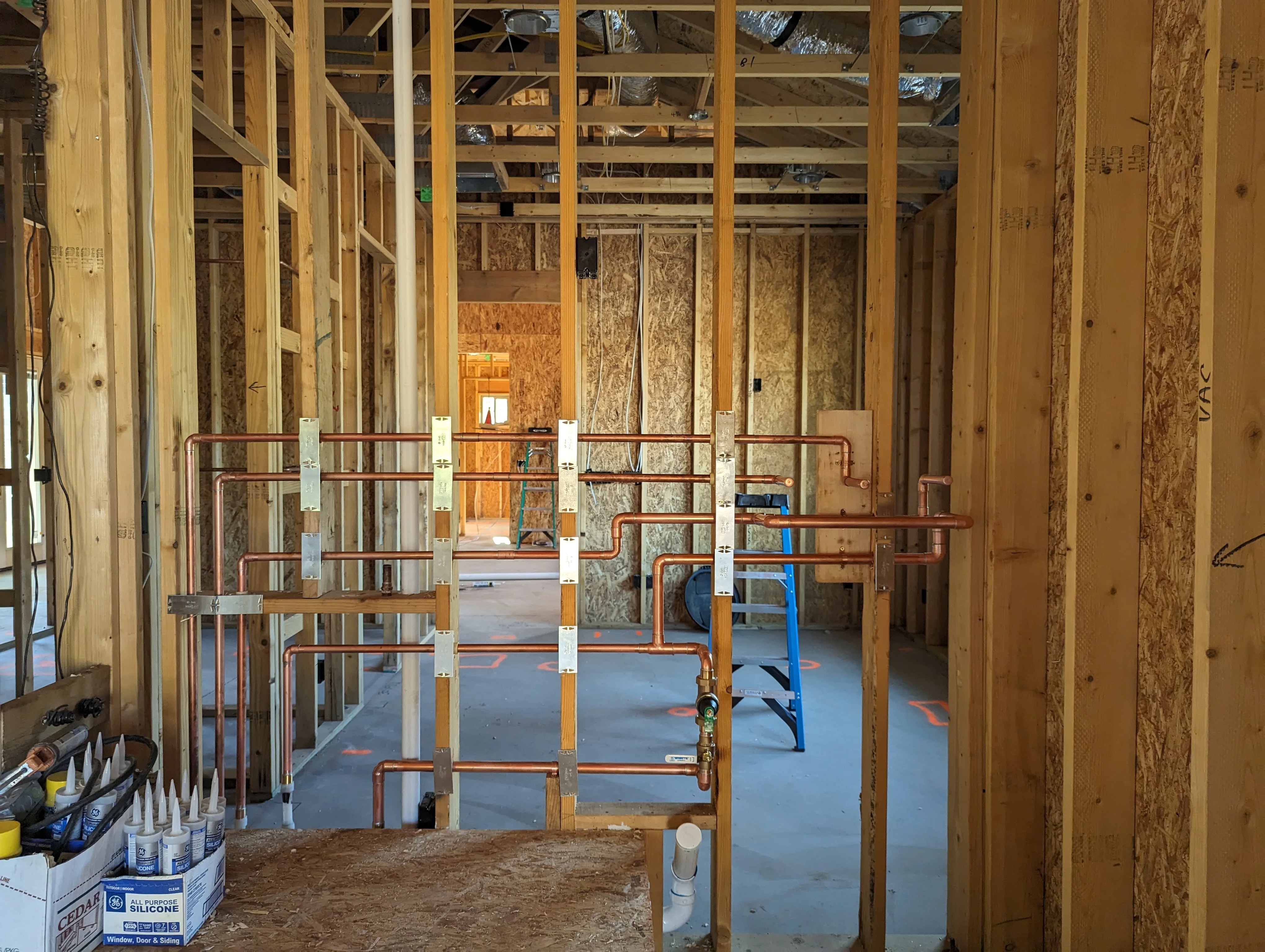 Copper and PVC plumbing lines installed in wood-framed residential construction with insulation and support straps