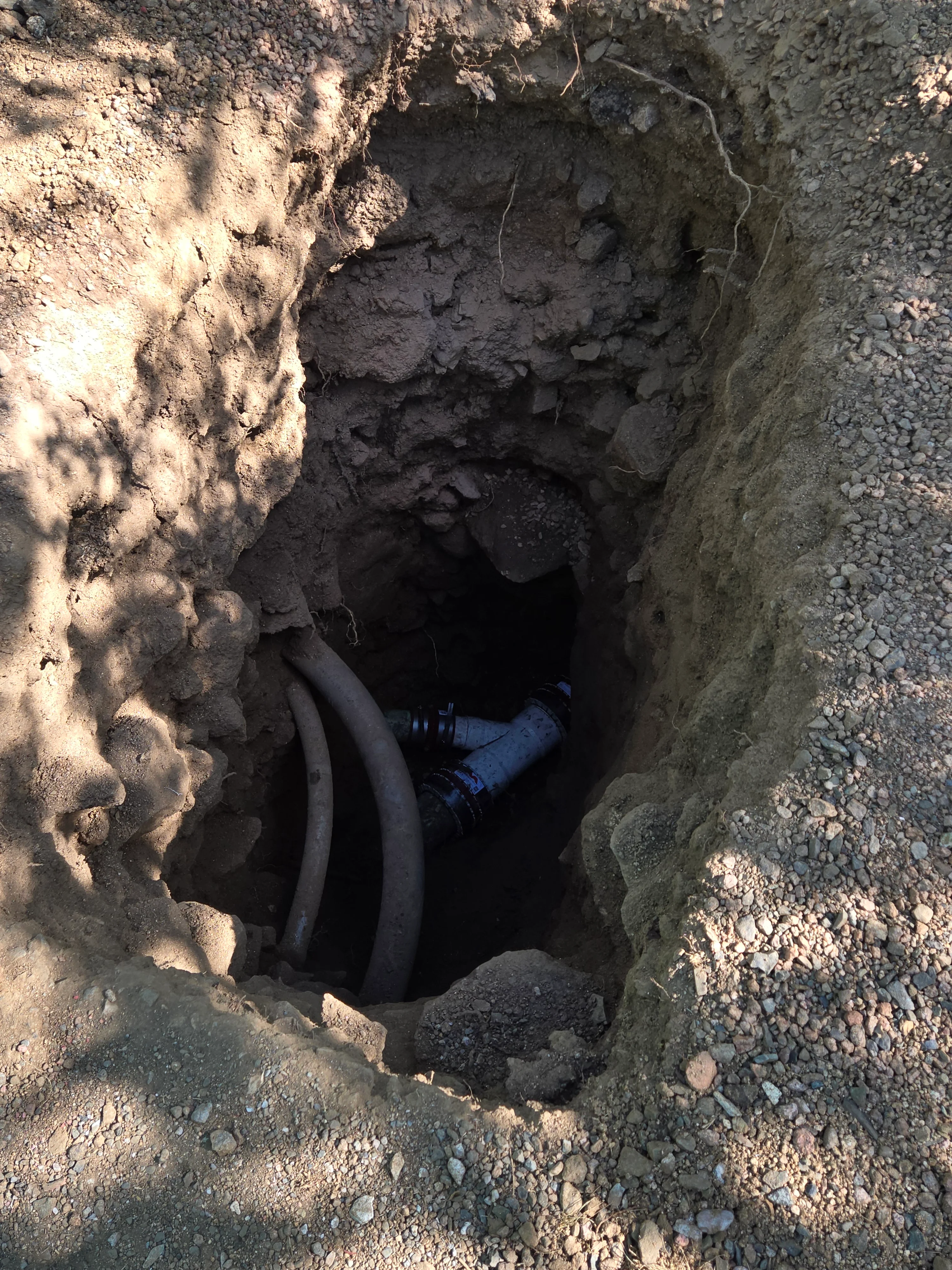Excavated sewer line trench with exposed black pipe and soil walls
